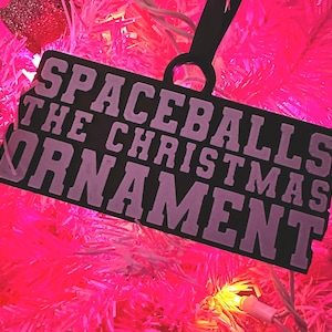 May include: Black Christmas ornament with white text that reads "Spaceballs The Christmas Ornament".