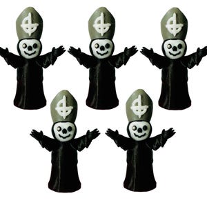 May include: Five small, black figurines of a character with a skull face, a tall hat with a white cross, and outstretched arms. The figurines are standing upright and have a smiling expression.