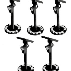 Puede incluir: Cinco modelos de cámaras de seguridad en miniatura de color blanco y negro sobre soportes. Cada unidad cuenta con un panel solar en la parte superior, una lente de cámara y una base circular con el texto ALWAYS WATCHING en relieve blanco.