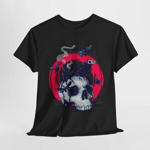 May include: Black t-shirt with a graphic of a skull with a crow perched on top. The skull is surrounded by a red circle with smoke coming from the top. There are also small black birds flying around the skull.