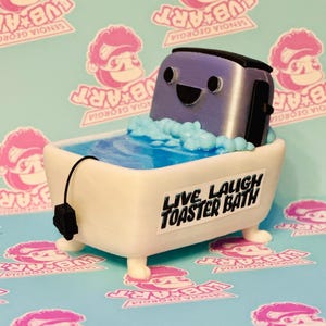 May include: A whimsical sculpture of a toaster in a bathtub. The purple toaster has a smiling face and is surrounded by blue bubbles. The white bathtub has the text "LIVE LAUGH TOASTER BATH" on the side. The background is a light blue pattern.