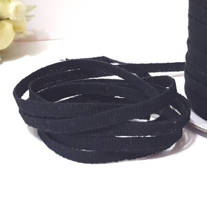 May include: A spool of black cotton twill tape. The tape is approximately 1/2 inch wide and is wound around a cardboard spool.