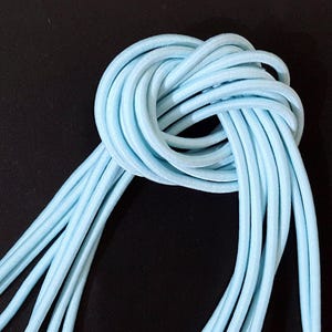 Könnte beinhalten: Ein Bündel hellblauer Gummikordel, etwa 10 Stränge, zu einem Knoten gebunden.