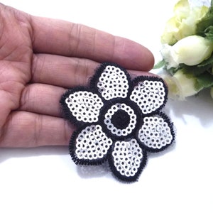 May include: A silver sequin flower applique with a black mesh backing. The flower has five petals and a centre circle.