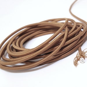 Könnte beinhalten: Eine Spule mit braunem, stoffbezogenem Stromkabel. Das Kabel ist fest gewickelt und das Ende des Kabels ist sichtbar.