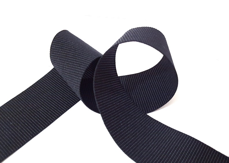 May include: Black grosgrain ribbon with a ribbed texture. The ribbon is folded in a loop shape.