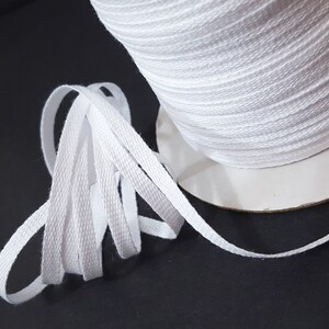 May include: A spool of white cotton twill tape. The tape is flat and woven with a subtle texture. It is wound around a cardboard spool.