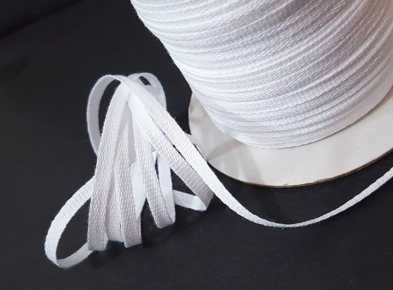 May include: A spool of white cotton twill tape. The tape is flat and woven with a subtle texture. It is wound around a cardboard spool.