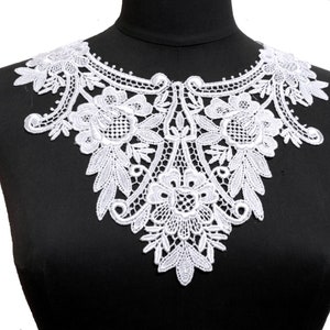 May include: A white lace collar with a floral design is displayed on a black mannequin. The collar features intricate detailing, including flowers and leaf patterns. The lace is delicate and appears to be made of a soft material.