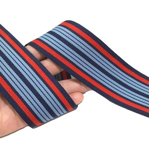 May include: Red and blue striped ribbon with a repeating pattern. The ribbon is woven with thin red and blue stripes.
