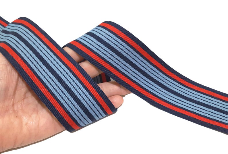 May include: Red and blue striped ribbon with a repeating pattern. The ribbon is woven with thin red and blue stripes.
