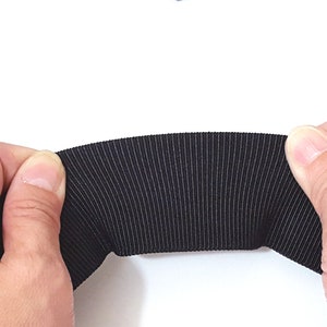 May include: Black elastic band with a ribbed texture. The band is being held in two hands.