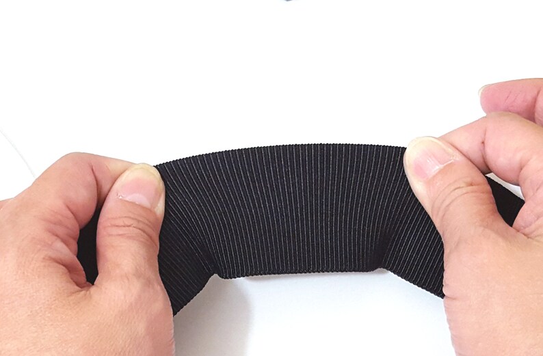 May include: Black elastic band with a ribbed texture. The band is being held in two hands.