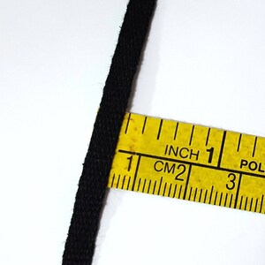 May include: Black fabric cord measured with a yellow tape measure marked in inches and centimeters. The tape measure reads "Inch 1 CM 2 3 4 POLYEST"