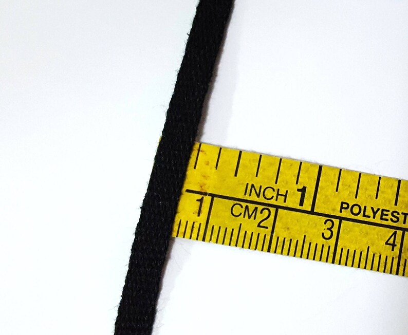 May include: Black fabric cord measured with a yellow tape measure marked in inches and centimeters. The tape measure reads "Inch 1 CM 2 3 4 POLYEST"