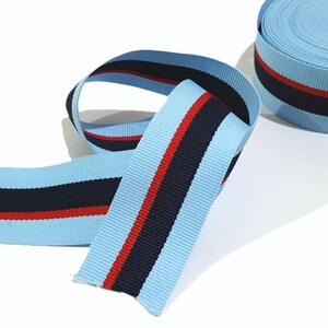 May include: Light blue ribbon with red and navy blue stripes. The ribbon is rolled up and ready to be used for crafts, decorations, or gift wrapping.