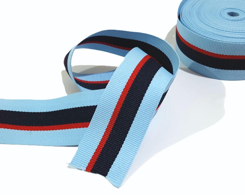 May include: Light blue ribbon with red and navy blue stripes. The ribbon is rolled up and ready to be used for crafts, decorations, or gift wrapping.