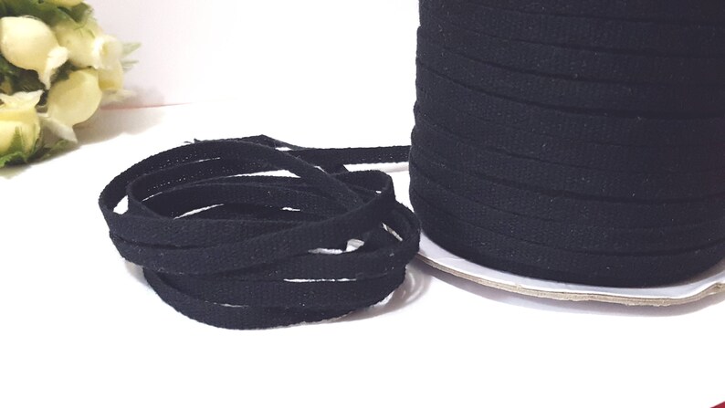 May include: A spool of black cotton twill tape. The tape is approximately 1/2 inch wide and is wound around a cardboard spool.