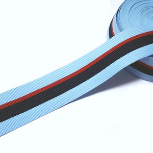 May include: A light blue ribbon with a black and red stripe. The ribbon is rolled up and ready to be used for crafts or decorations.