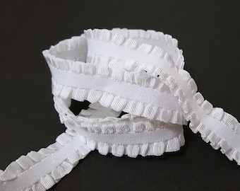 May include: White ruffled elastic trim. The trim is made of a soft, white fabric with a ruffled edge. It is perfect for adding a touch of elegance to any project.