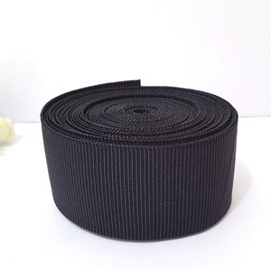 May include: A roll of black grosgrain ribbon. The ribbon is tightly wound and has a smooth, shiny finish.