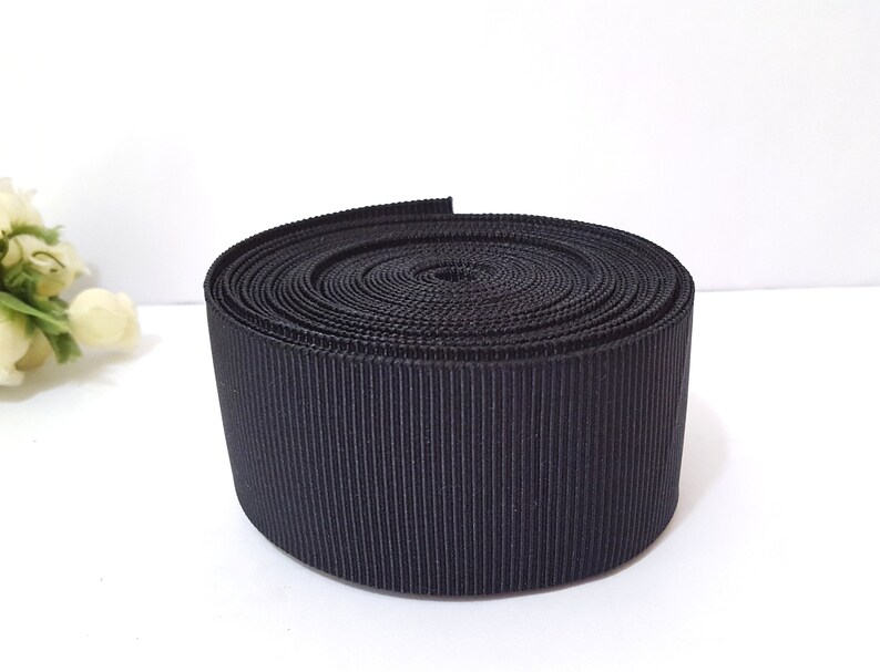 May include: A roll of black grosgrain ribbon. The ribbon is tightly wound and has a smooth, shiny finish.