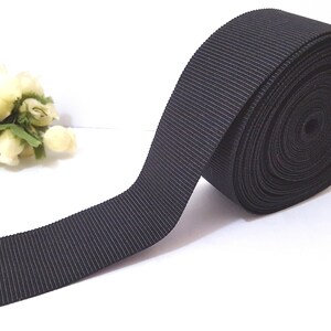 May include: A roll of black grosgrain ribbon. The ribbon is flat and has a ribbed texture.