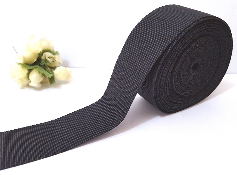 May include: A roll of black grosgrain ribbon. The ribbon is flat and has a ribbed texture.