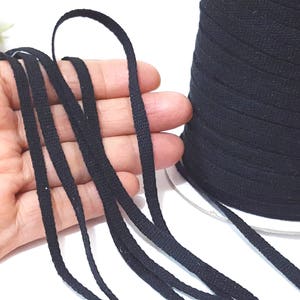 May include: Black cotton cord, a spool of the cord, and several strands of the cord laid out on a hand.