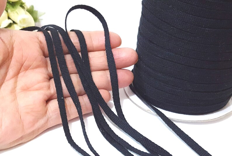 May include: Black cotton cord, a spool of the cord, and several strands of the cord laid out on a hand.