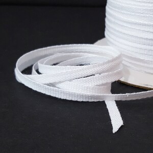 May include: White cotton twill tape, a type of ribbon, is wound on a spool. The tape is flat and has a subtle herringbone weave.