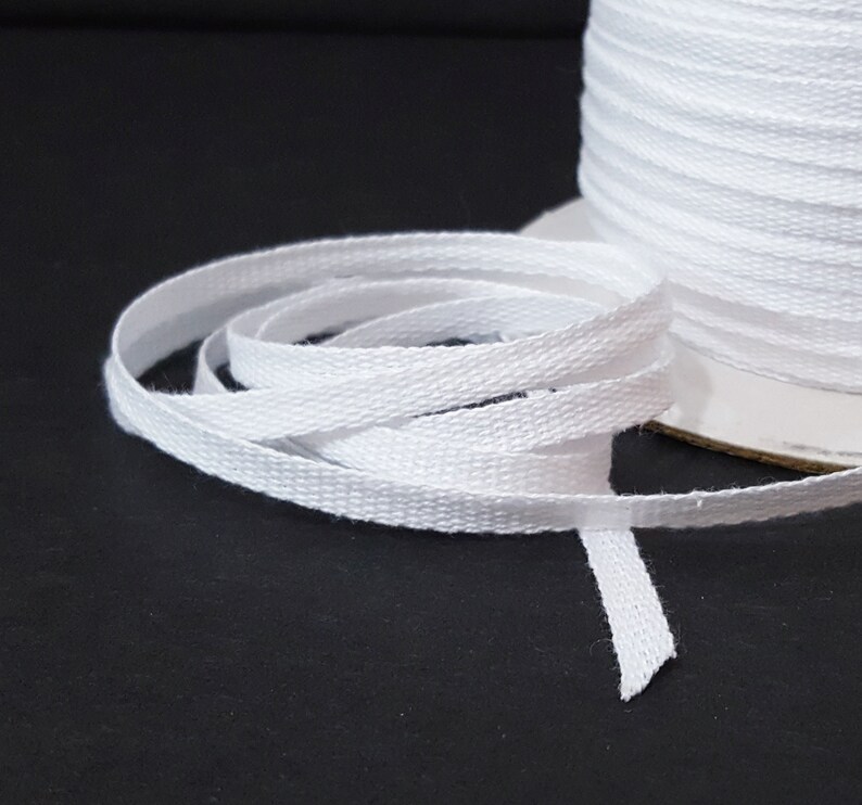 May include: White cotton twill tape, a type of ribbon, is wound on a spool. The tape is flat and has a subtle herringbone weave.