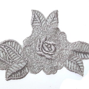 May include: Silver embroidered lace applique with a floral design featuring two roses and leaves.
