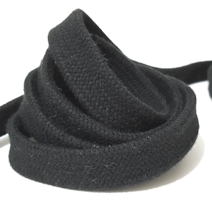 May include: Black cotton cord, a thick, braided rope-like material, is coiled and folded on a white surface. The cord is approximately 1.2 cm in diameter.