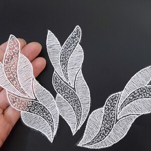 Könnte beinhalten: Vier weiße Spitzenapplikationen in Blattform. Die Applikationen sind zart und filigran mit einem floralen Design.