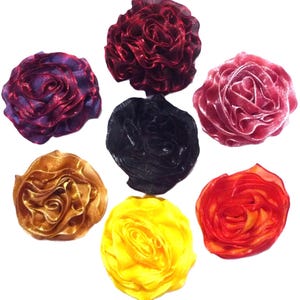 Może przedstawiać: Kolekcja siedmiu materiałowych ozdób kwiatowych w różnych kolorach. Kwiaty obejmują odcienie czerwieni, fioletu, złota, żółci i czerni. Każdy kwiat ma pofałdowany, warstwowy wzór, przypominający różę.