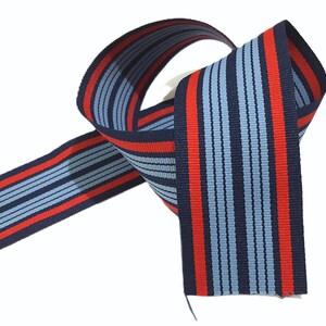 May include: Red and blue striped ribbon with a woven texture. The ribbon is approximately 1 inch wide.