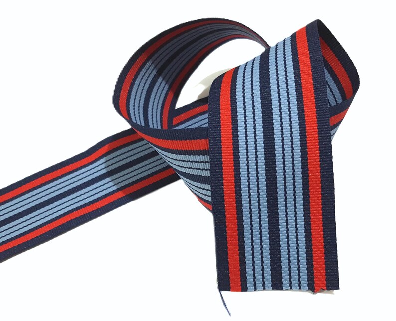 May include: Red and blue striped ribbon with a woven texture. The ribbon is approximately 1 inch wide.