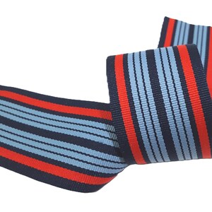May include: Red and blue striped ribbon with a woven design. The ribbon is folded in half and the stripes are running vertically.