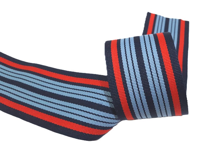 May include: Red and blue striped ribbon with a woven design. The ribbon is folded in half and the stripes are running vertically.