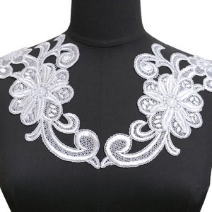 May include: White lace trim with a floral design. The trim is made of delicate lace and features a large flower in the centre. The trim is perfect for adding a touch of elegance to any garment.