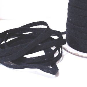 May include: A spool of black cotton twill tape. The tape is approximately 1/2 inch wide and is wound around a white cardboard spool.