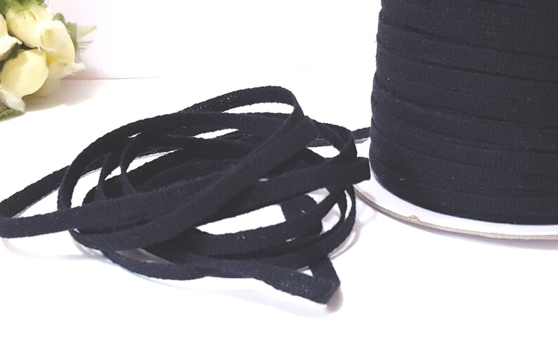 May include: A spool of black cotton twill tape. The tape is approximately 1/2 inch wide and is wound around a white cardboard spool.