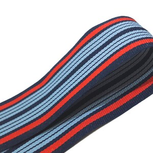 May include: Red, blue, and light blue striped ribbon. The ribbon is folded in half and the stripes are running vertically.