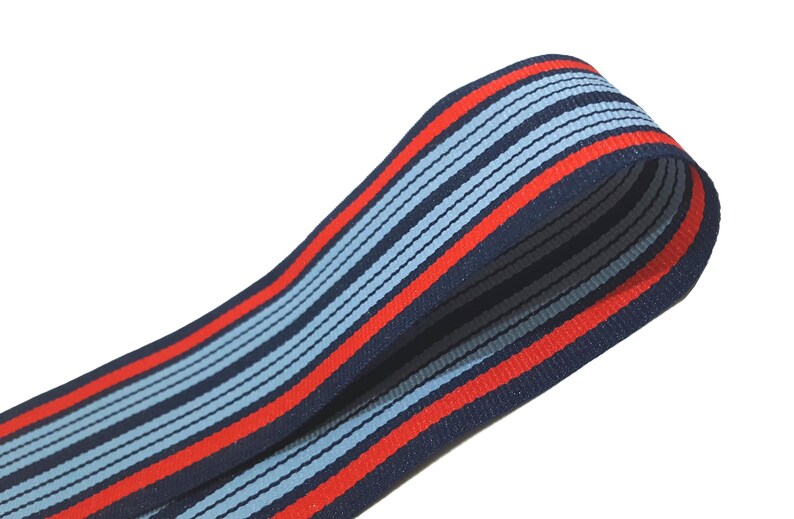 May include: Red, blue, and light blue striped ribbon. The ribbon is folded in half and the stripes are running vertically.