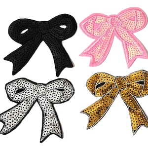 May include: Four sequined bow appliques in black, pink, silver, and gold. The bows are all the same size and shape, and they are perfect for adding a touch of sparkle to any project.
