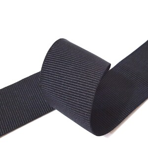 May include: Black grosgrain ribbon with a ribbed texture. The ribbon is rolled up and the ends are visible.