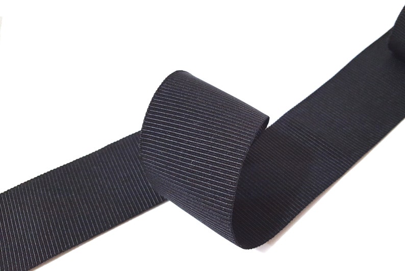 May include: Black grosgrain ribbon with a ribbed texture. The ribbon is rolled up and the ends are visible.