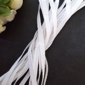 May include: A bundle of white cotton twill tape, arranged in a criss-cross pattern on a black background.