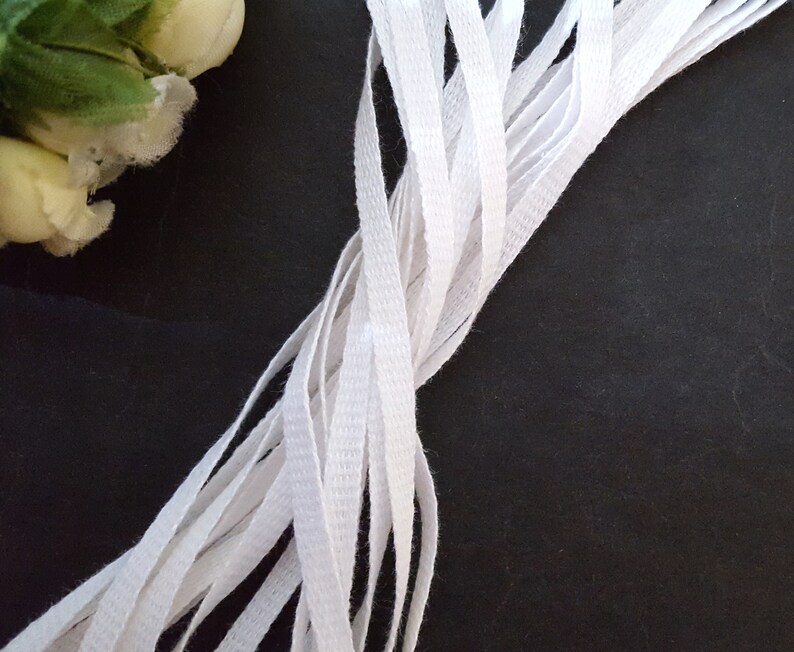 May include: A bundle of white cotton twill tape, arranged in a criss-cross pattern on a black background.